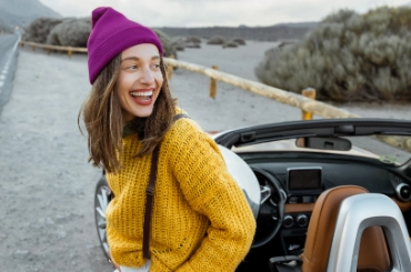 Frau steht mit ihrem Cabriolet seitlich bei einer Strasse und lacht
