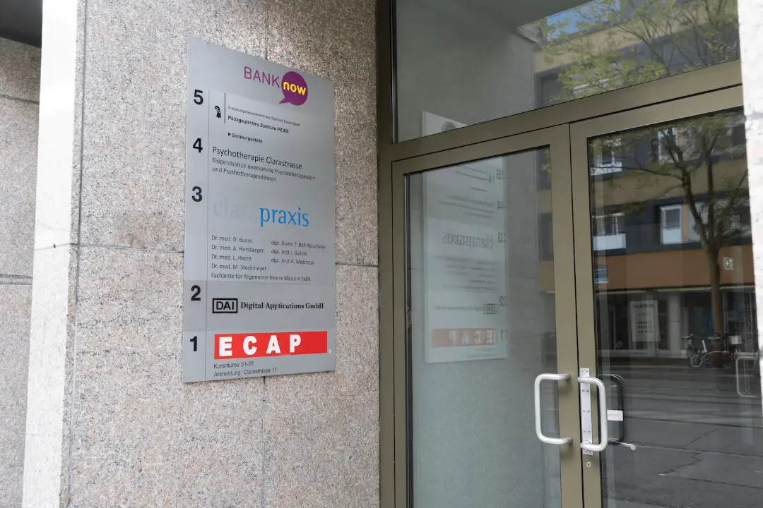 Eingangsbereich der BANK-now Filiale Basel mit Filialschildern und benachbarten Geschäften.