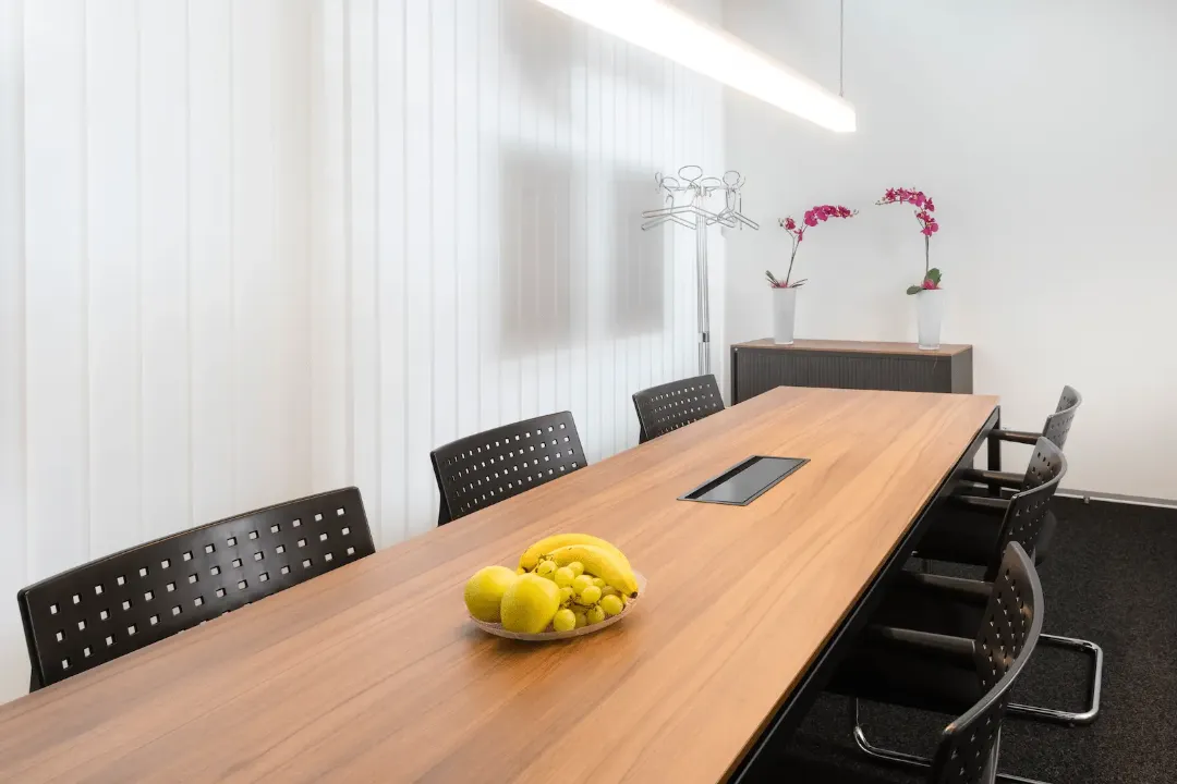 Besprechungsraum der BANK-now Filiale Uster mit langem Tisch, mehreren Stühlen und Orchidee im Hintergrund.