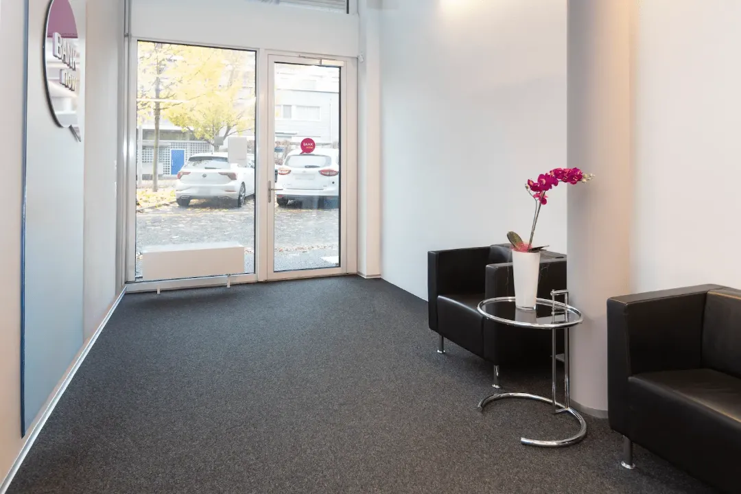 Heller Eingangsbereich der BANK-now Filiale Uster mit zwei Sesseln, Tisch und grossen Fenstern.