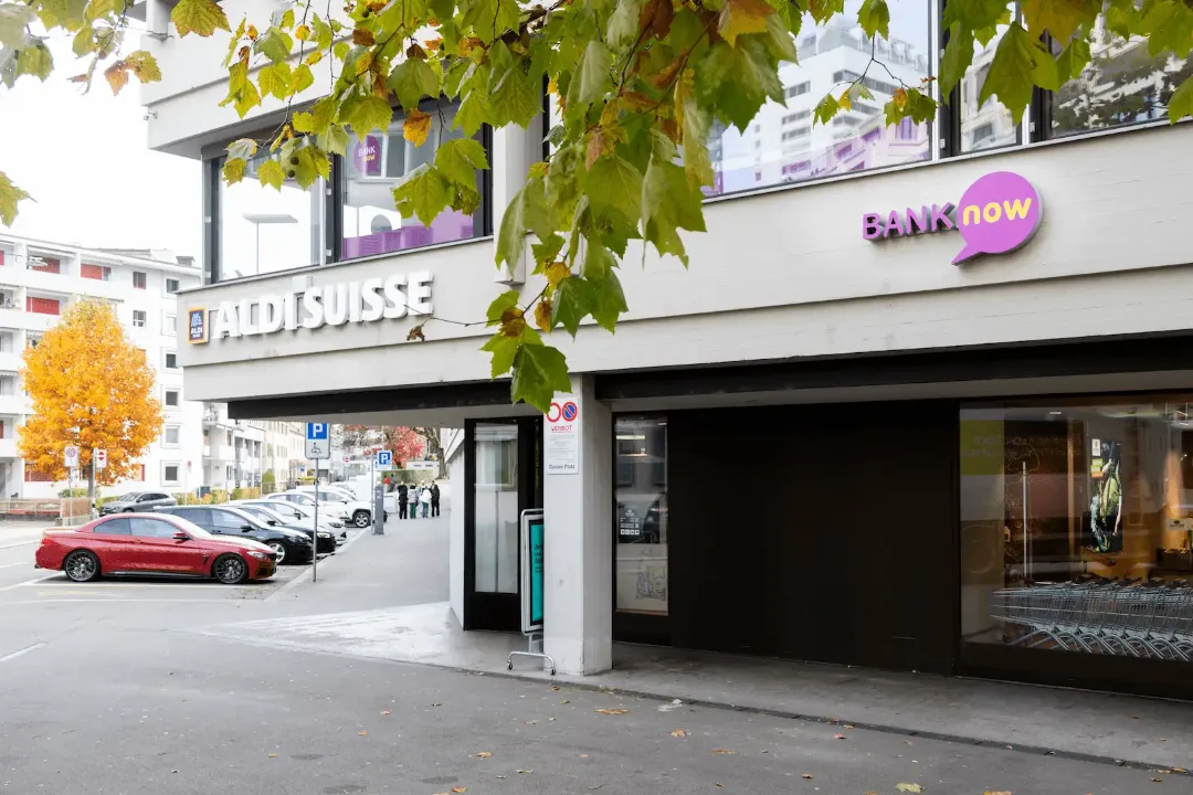 Exterior view of the BANK-now Zurich-Oerlikon branch with entrance, BANK-now logo and street view.