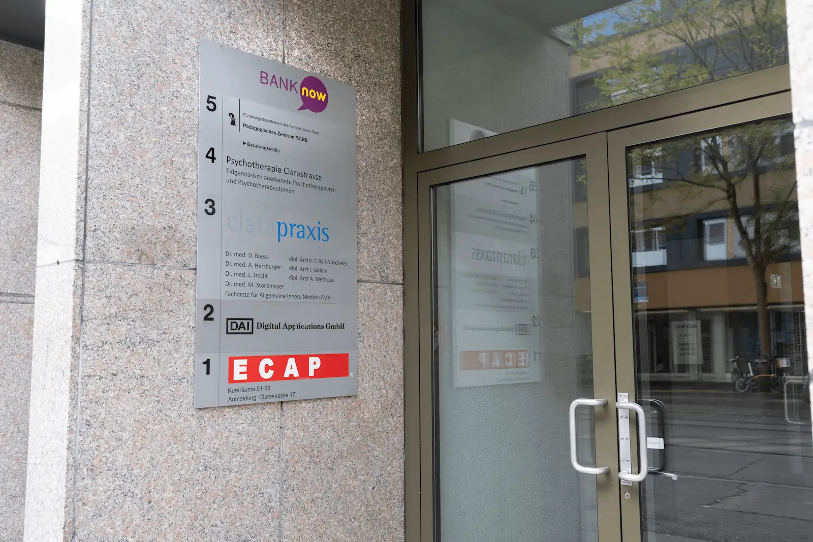 Eingangsbereich der BANK-now Filiale Basel mit Filialschildern und benachbarten Geschäften.
