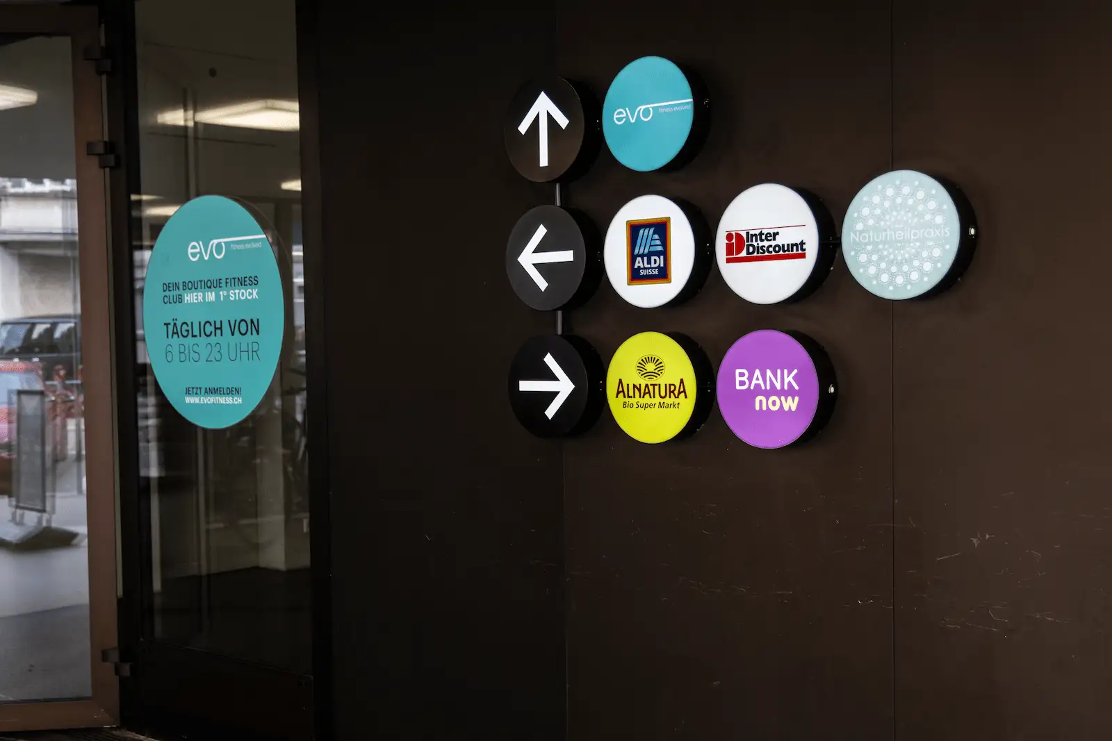 Signage at the entrance of the BANK-now Zurich-Oerlikon branch with logos and directional arrows.