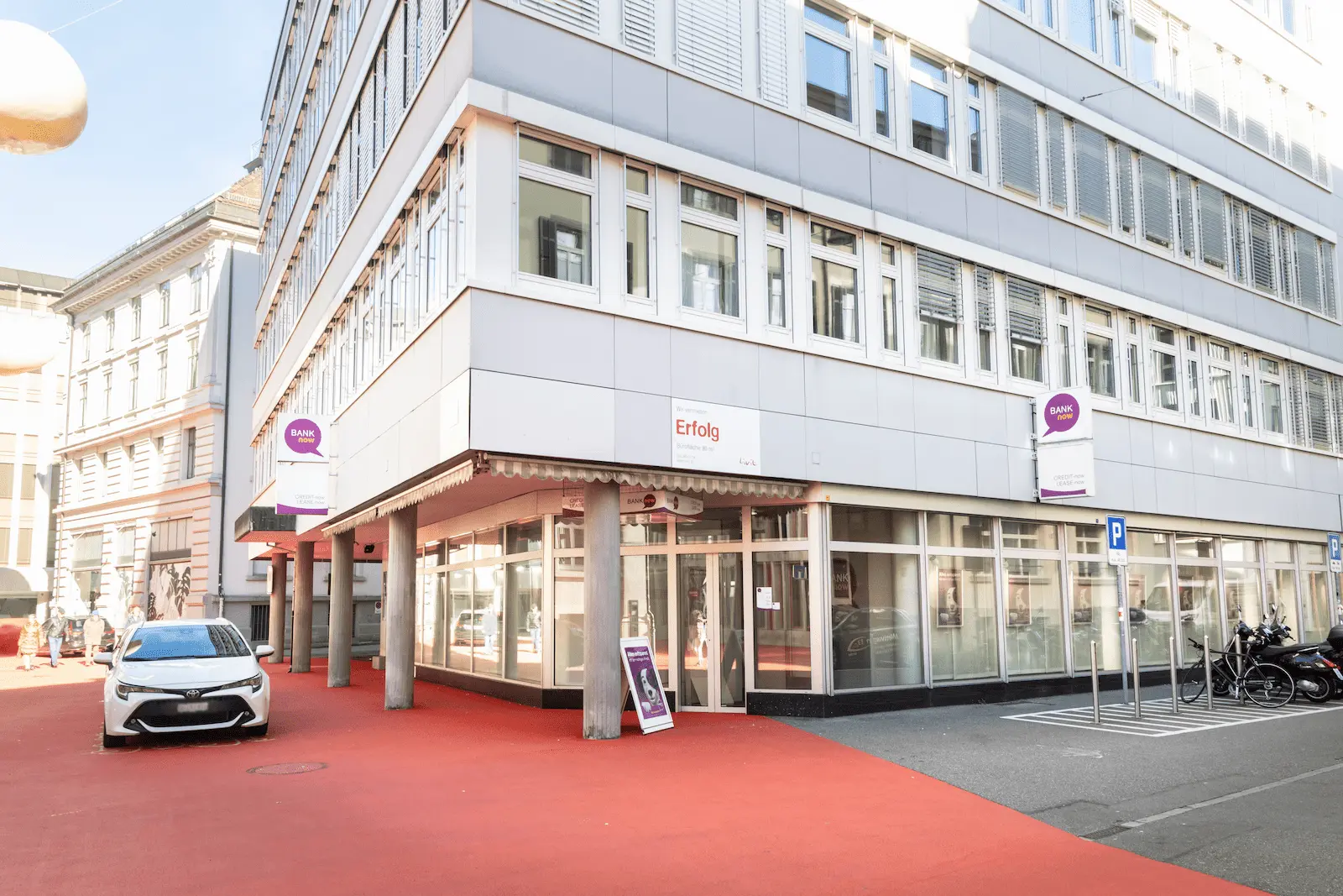 Zweite Aussenansicht der BANK-now Filiale St. Gallen mit Gebäudeecke, Eingang und sichtbarer Signaletik.