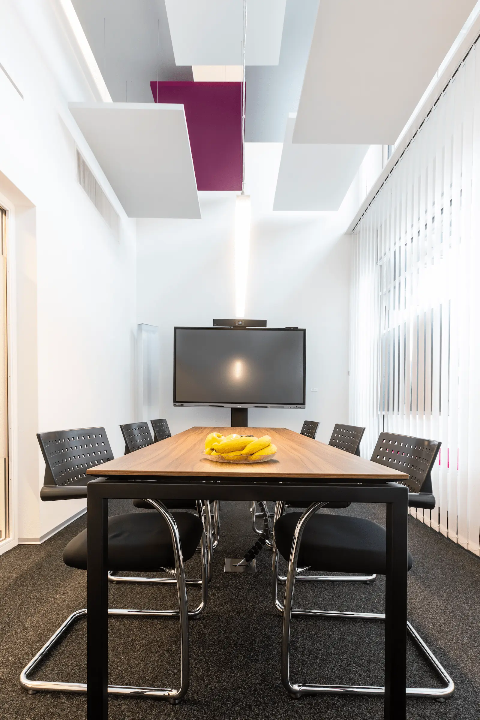 Grosser Besprechungsraum der BANK-now Filiale Uster mit langem Tisch, Stühlen, Bildschirm und modernen Akustikelementen an der Decke.